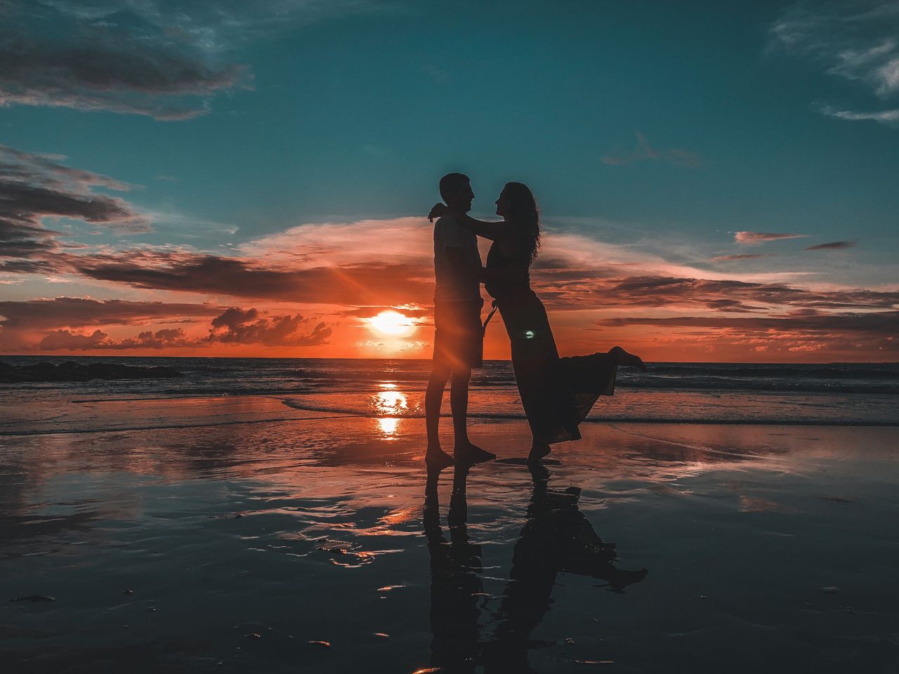 Silhouette of a couple embracing on a Bali beach during a breathtaking sunset, symbolizing love and tranquility.